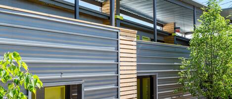 A modern building with a metal exterior, a covered outdoor area, and a small garden with stepping stones.