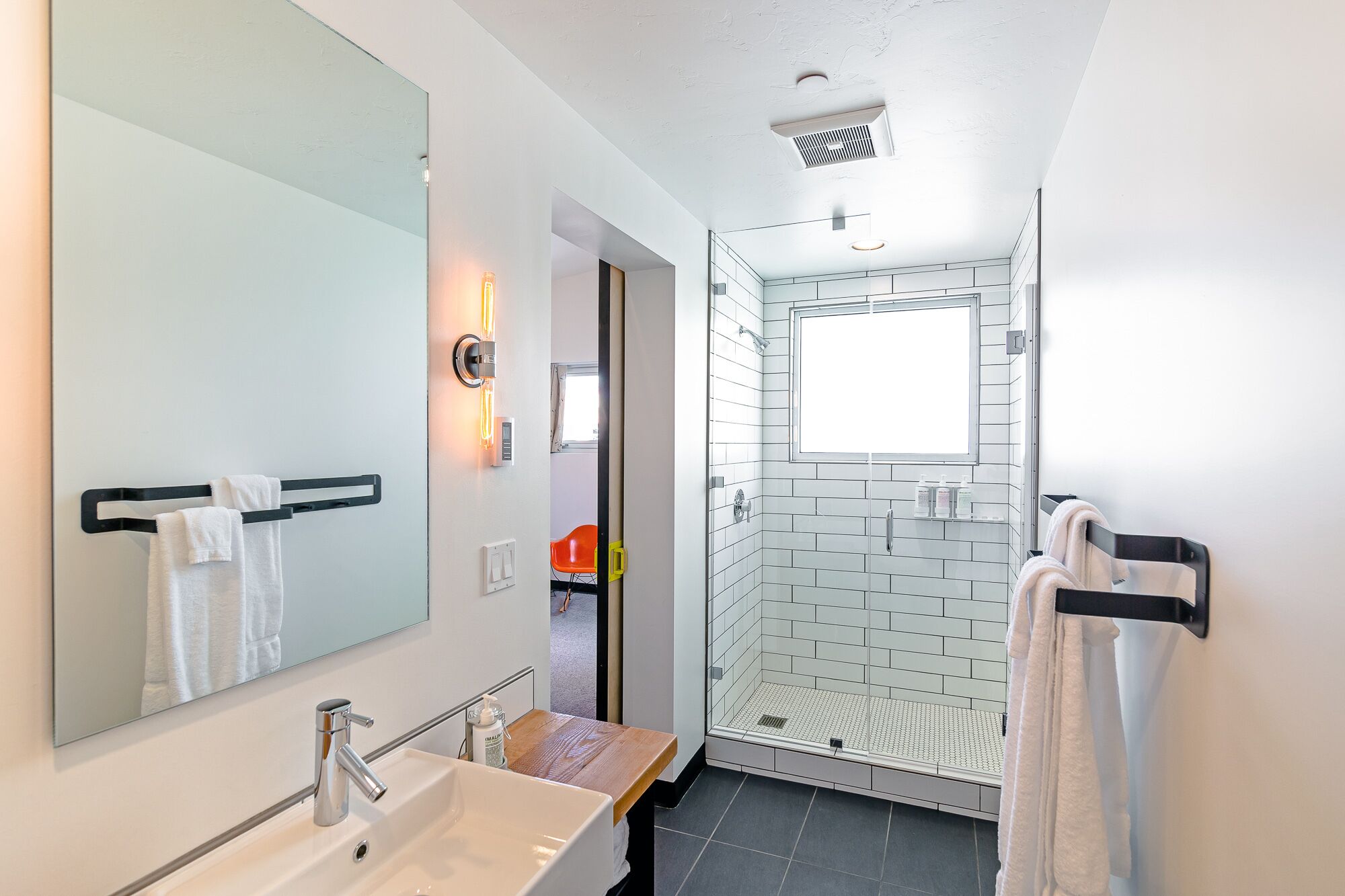 A modern bathroom with a large mirror, white sink, and a glass shower enclosure.