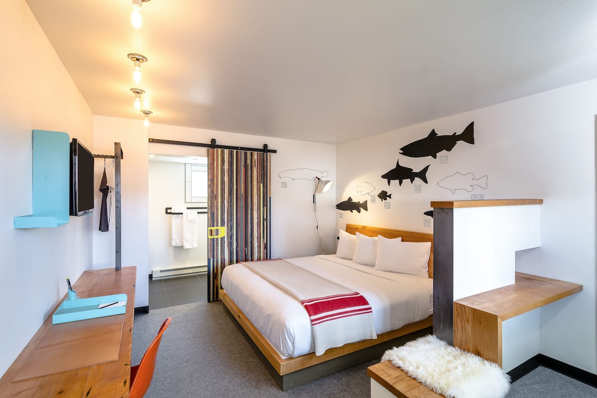 Ett modernt hotellrum med en säng i trä, ett skrivbord och utsikt över korridoren.