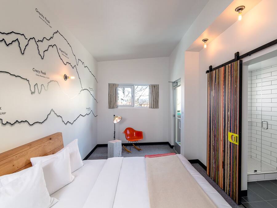 A modern hotel room with a large bed, a map on the wall, a red chair, and a sliding door.
