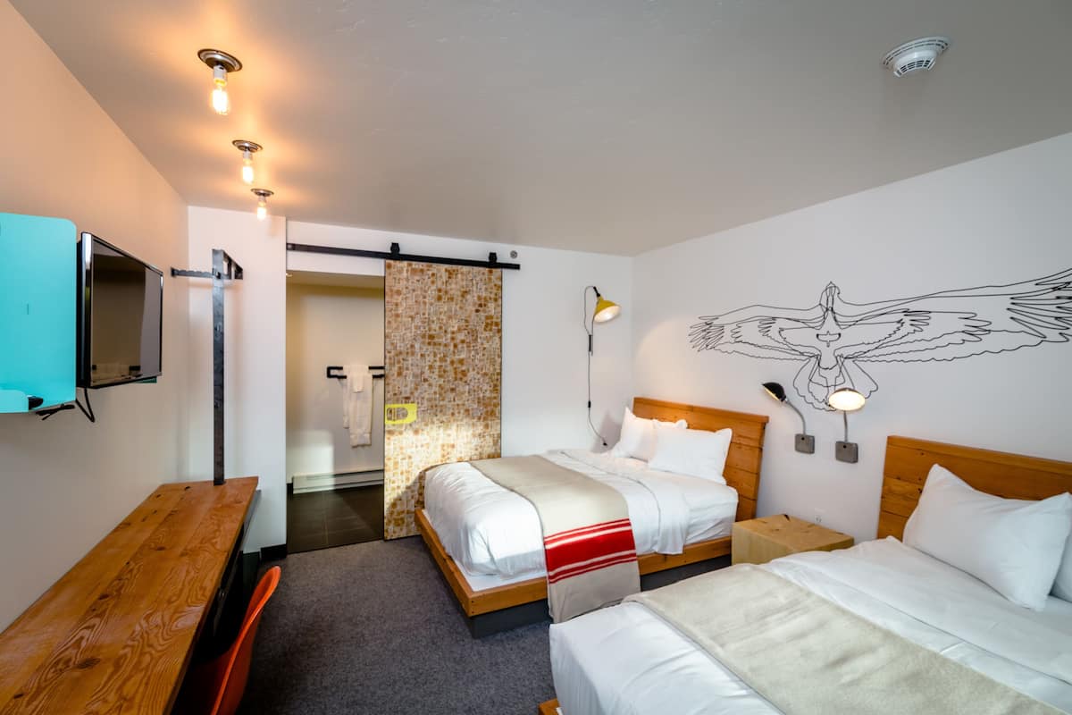 Ett hotellrum med två sängar, ett skrivbord i trä, en TV och en väggmålning med vingar på väggen.