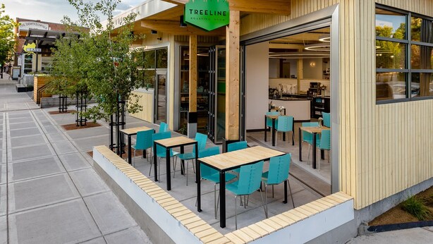 Un edificio moderno con fachada de madera, zona de estar al aire libre y un letrero que dice 'TREELINE ROASTING ROOM'.