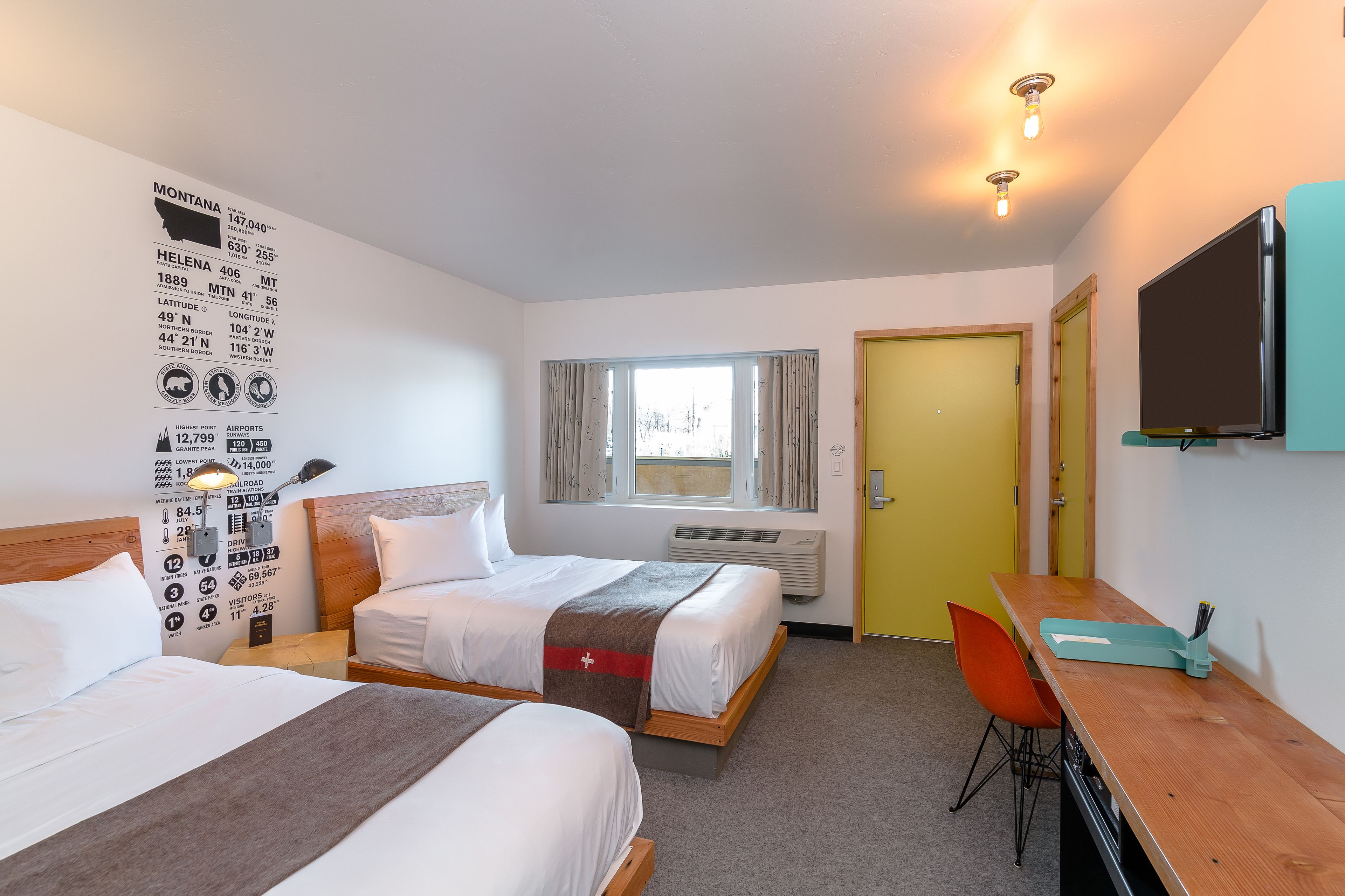 A hotel room with two beds, a desk, a TV, and a window with curtains.