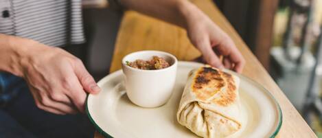 Una persona sosteniendo un plato con un wrap y un recipiente pequeño con salsa.