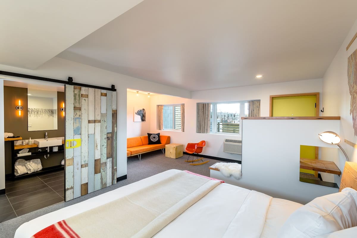 Ett modernt hotellrum med en stor säng, en soffa, ett skrivbord och ett badrum med handfat och spegel.
