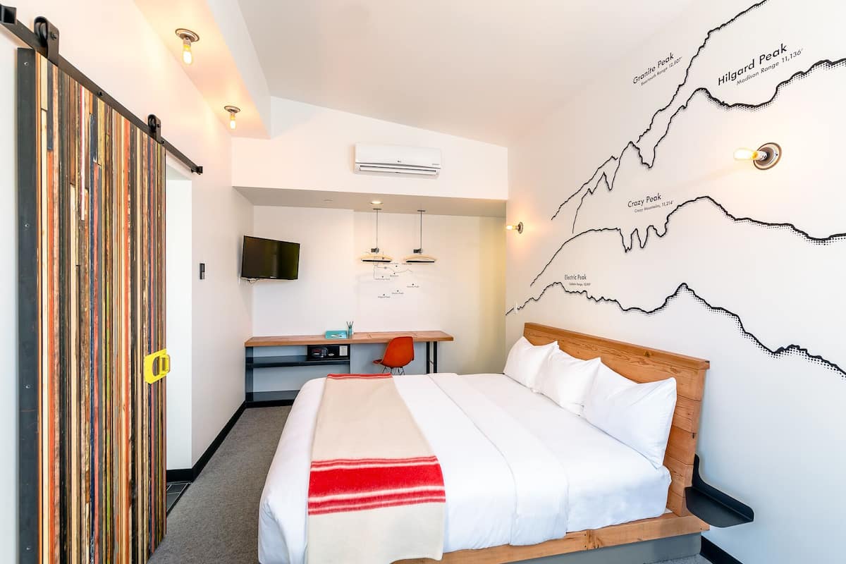 Ett hotellrum med en säng, ett skrivbord och en väggkarta över berg.