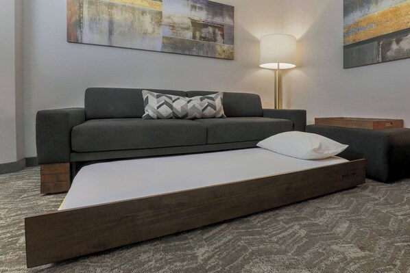 A modern room with a grey sofa, a wooden bed frame, and a floor lamp.