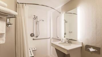 A bathroom with a shower, grab bars, a sink, and a mirror.