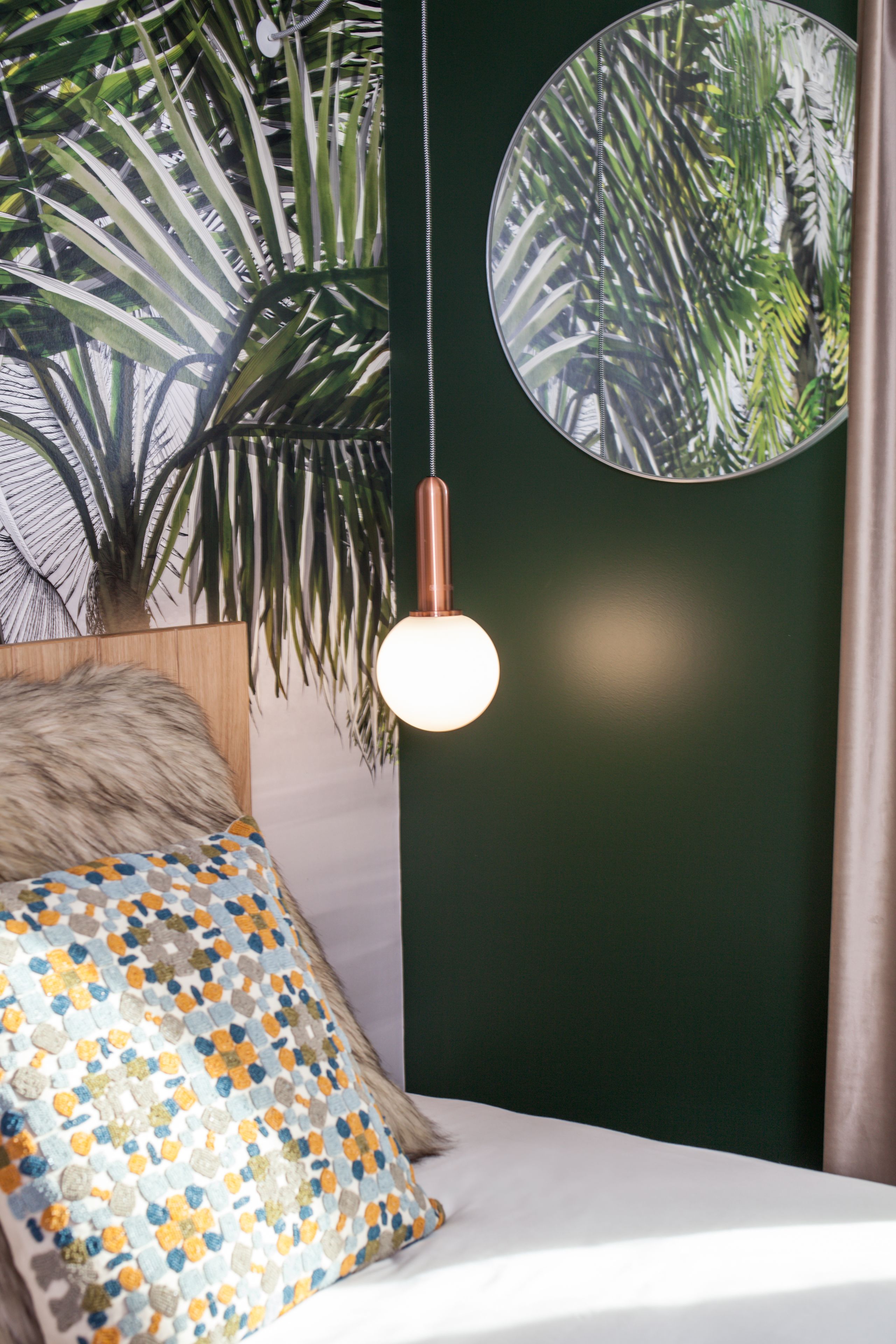 A bedroom with a bed, a round mirror, a hanging light fixture, and a potted plant.
