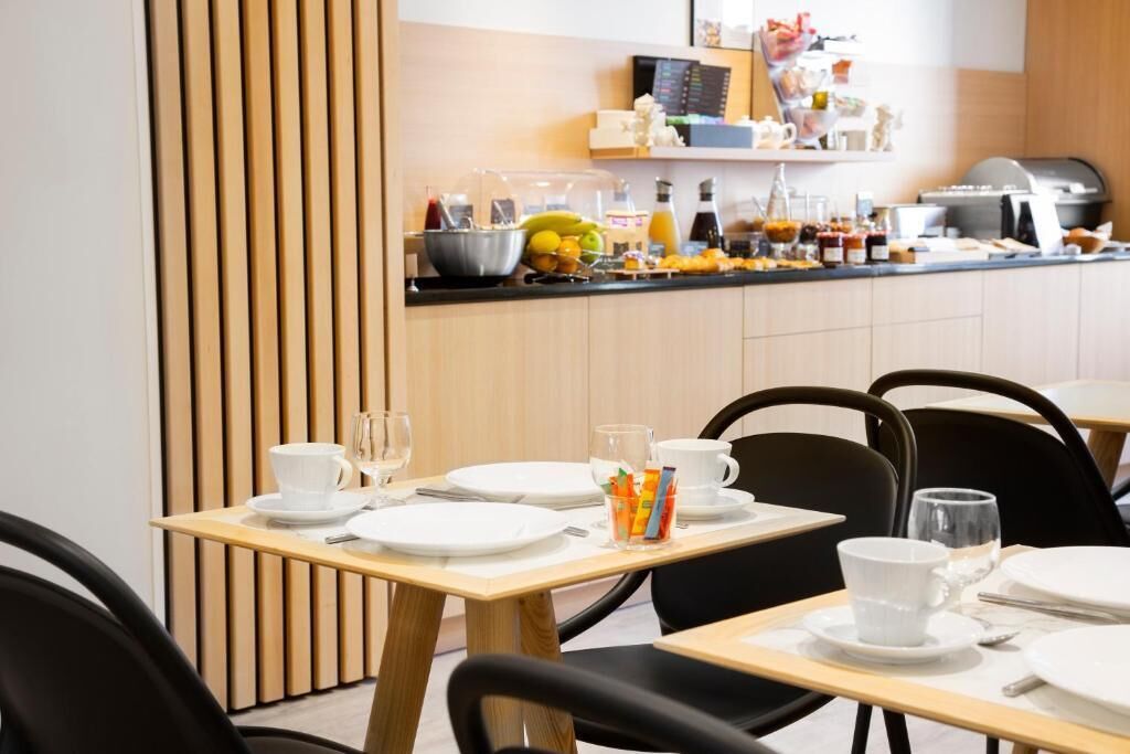 Un comedor con mesas dispuestas para comer, una cocina al fondo y un revestimiento de listones de madera.