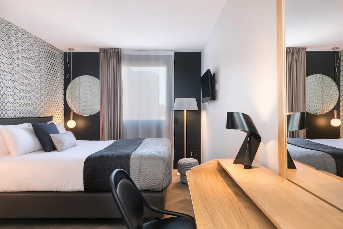 Una habitación de hotel moderna con dos camas, un escritorio, una silla, un televisor y un espejo grande.