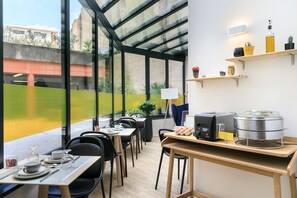 A modern dining area with glass walls, a buffet setup, and outdoor views. - Hotel Innes by HappyCulture (Toulouse)