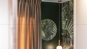 Un dormitorio con cama, cortinas, lámpara colgante y una pared con espejo circular y planta.