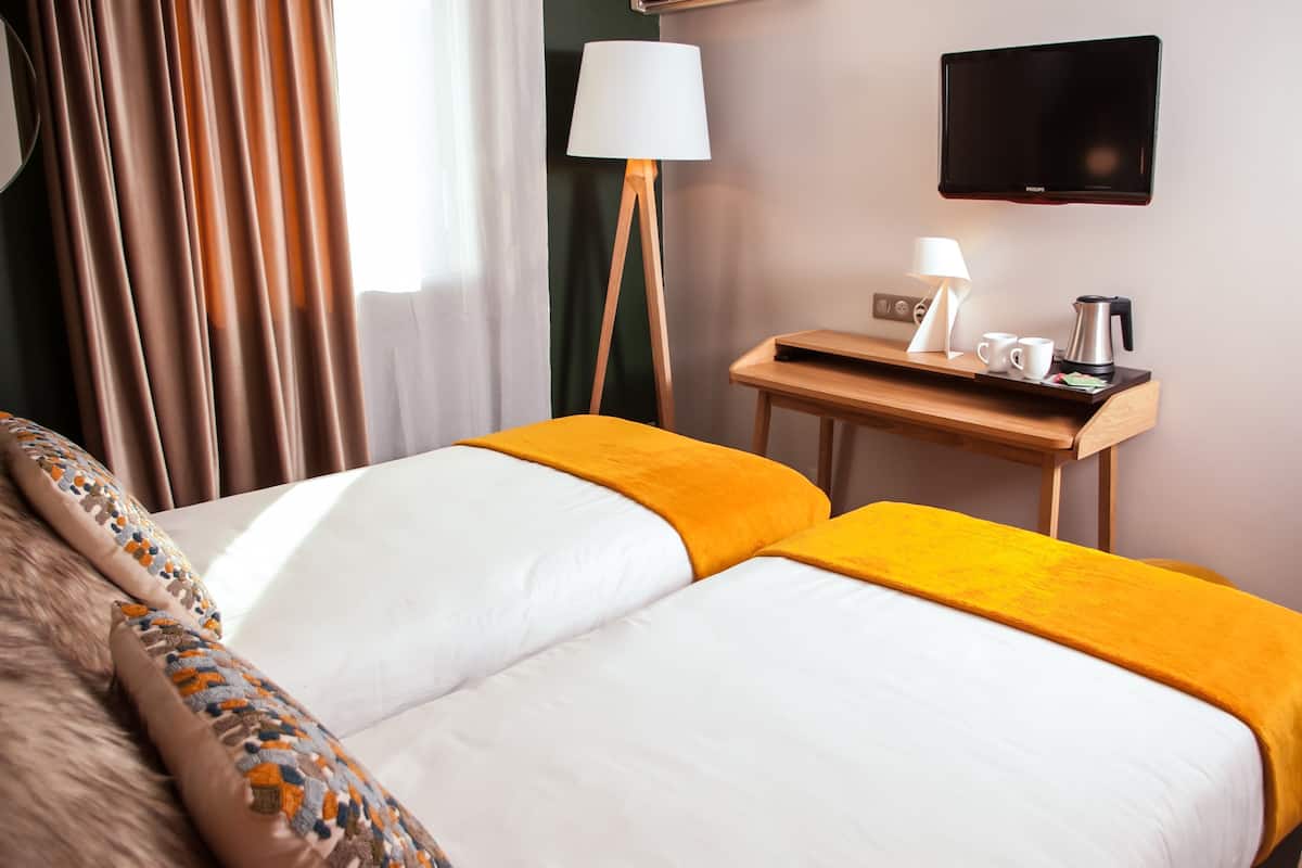 Habitación de hotel con cama, mesita de noche con lámpara, cafetera y televisión de pantalla plana.