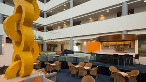 A spacious lobby with multiple seating areas, a large yellow sculpture, and a bar with a curved counter.