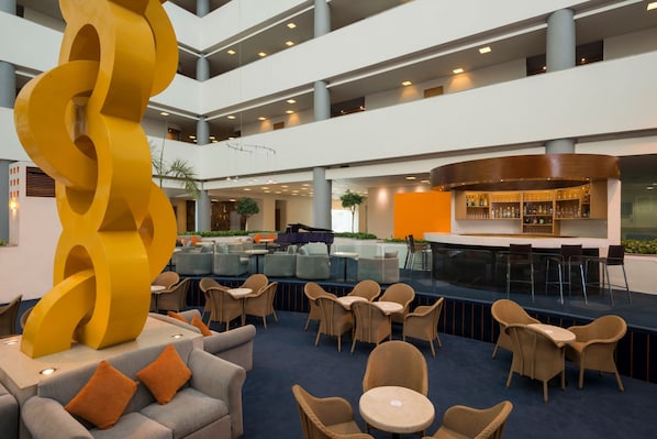 A spacious lobby with multiple seating areas, a large yellow sculpture, and a bar with a curved counter.