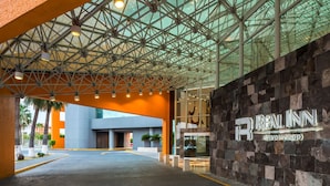 A hotel entrance with a modern glass ceiling, a prominent sign, and a paved walkway.