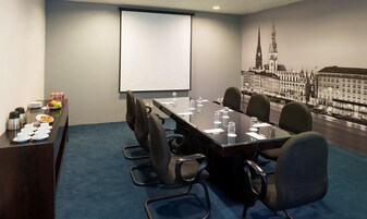 Una sala de conferencias con una larga mesa, sillas, una pantalla de proyector y un mural con vista a la ciudad.