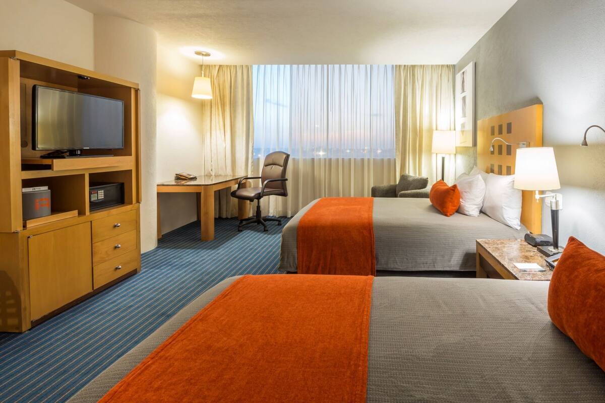 Habitación de hotel con dos camas, un escritorio, un televisor y una ventana con cortinas.