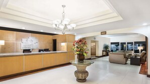 Ein Hotel-Empfangsbereich mit einer Rezeption, einem Chandelier, einer Vase mit Blumen und einer Sitzecke mit Sofas und einem Couchtisch.
