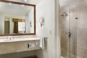 Une salle de bain dotée d’un grand miroir, d’un lavabo à deux robinets, d’un porte-serviettes et d’une douche à parois de verre.