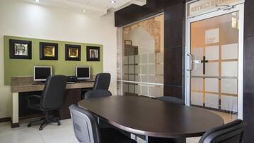 A conference room with a large oval table, four chairs, two computer monitors, and framed pictures on the wall.