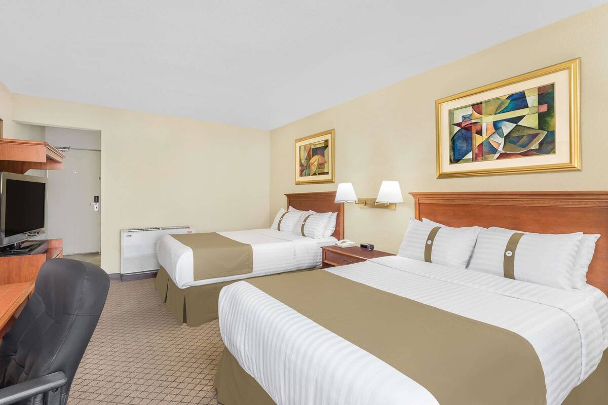A hotel room with two beds, a desk, a chair, and artwork on the walls.