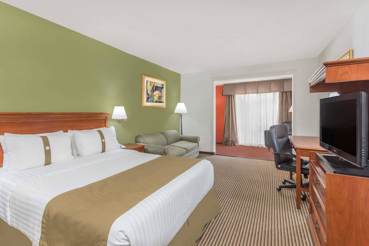 A hotel room with a large bed, a desk with a television, a sofa, and a painting on the wall.