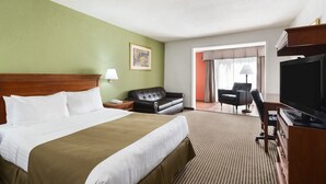 Ein Hotelzimmer mit einem großen Bett, einem Schreibtisch mit Fernseher, einer Couch und einem Sessel.