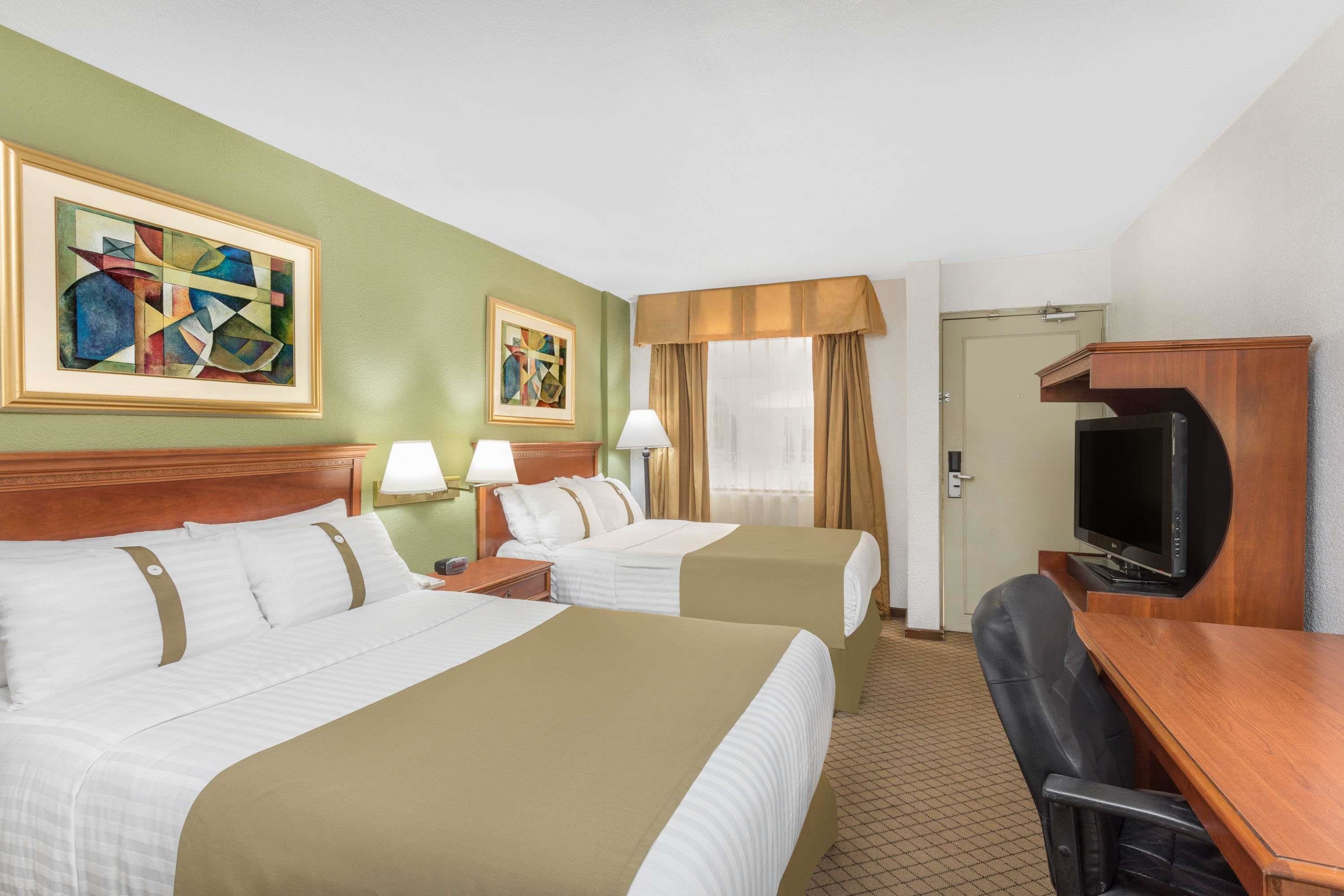 A hotel room with two beds, a desk, a television, and artwork on the walls.