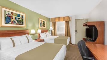 A hotel room with two beds, a desk, a television, and artwork on the walls.