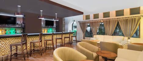A bar area with wooden chairs, a counter with a TV, and a seating area with sofas and tables.