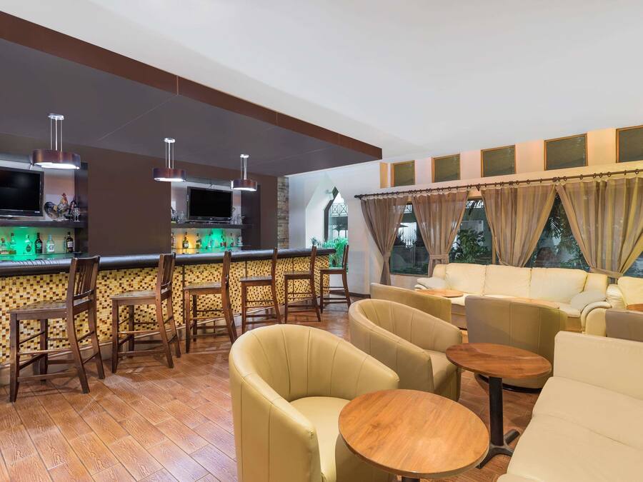 Zona de bar con sillas de madera, una barra con televisor y un área de estar con sofás y mesas.
