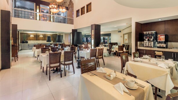 Eine großzügige Hotelhalle mit mehreren Gastronomiebereichen, einem sichtbaren Küchenbereich und einer Zwischenebene.