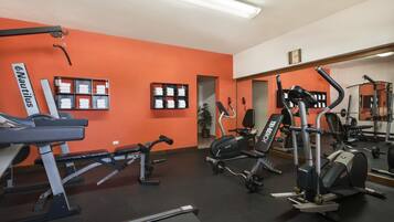 Un gimnasio con diversos equipos de ejercicio, incluyendo cintas de correr y máquinas de pesas, y un espejo que refleja el equipo.