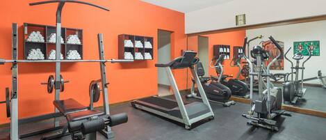 A gym with orange walls, weightlifting equipment, treadmills, and exercise machines.