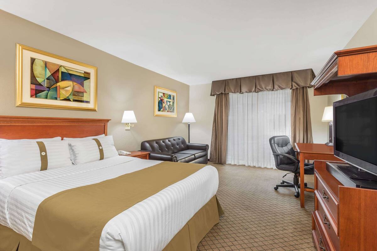 A hotel room with a large bed, two bedside tables, a desk with a television, a leather sofa, and two paintings on the wall.