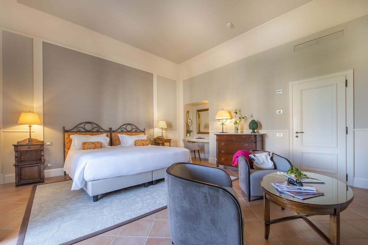 Una habitación de hotel con una cama grande, un escritorio, una silla, una mesita y un aparador.