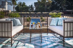 A balcony with two sofas, a glass table with a drink and a vase, and a tiled floor. - Almar Giardino di Costanza Mazara del Vallo Resort & Spa (Mazara del Vallo)