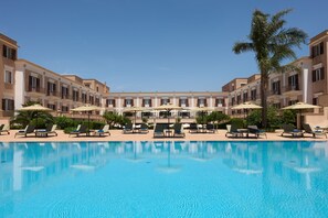 A swimming pool with lounge chairs and umbrellas, surrounded by a multi-story building with balconies. - Almar Giardino di Costanza Mazara del Vallo Resort & Spa (Mazara del Vallo)