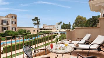 Ein Balkon mit Liegestühlen, ein Tisch mit Getränken, ein Pool und Blick auf ein Gebäude und Grünflächen.