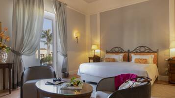Habitación de hotel con una cama, dos mesitas de noche con lámparas, una mesa redonda de vidrio, una silla y vistas a palmeras a través de la ventana.
