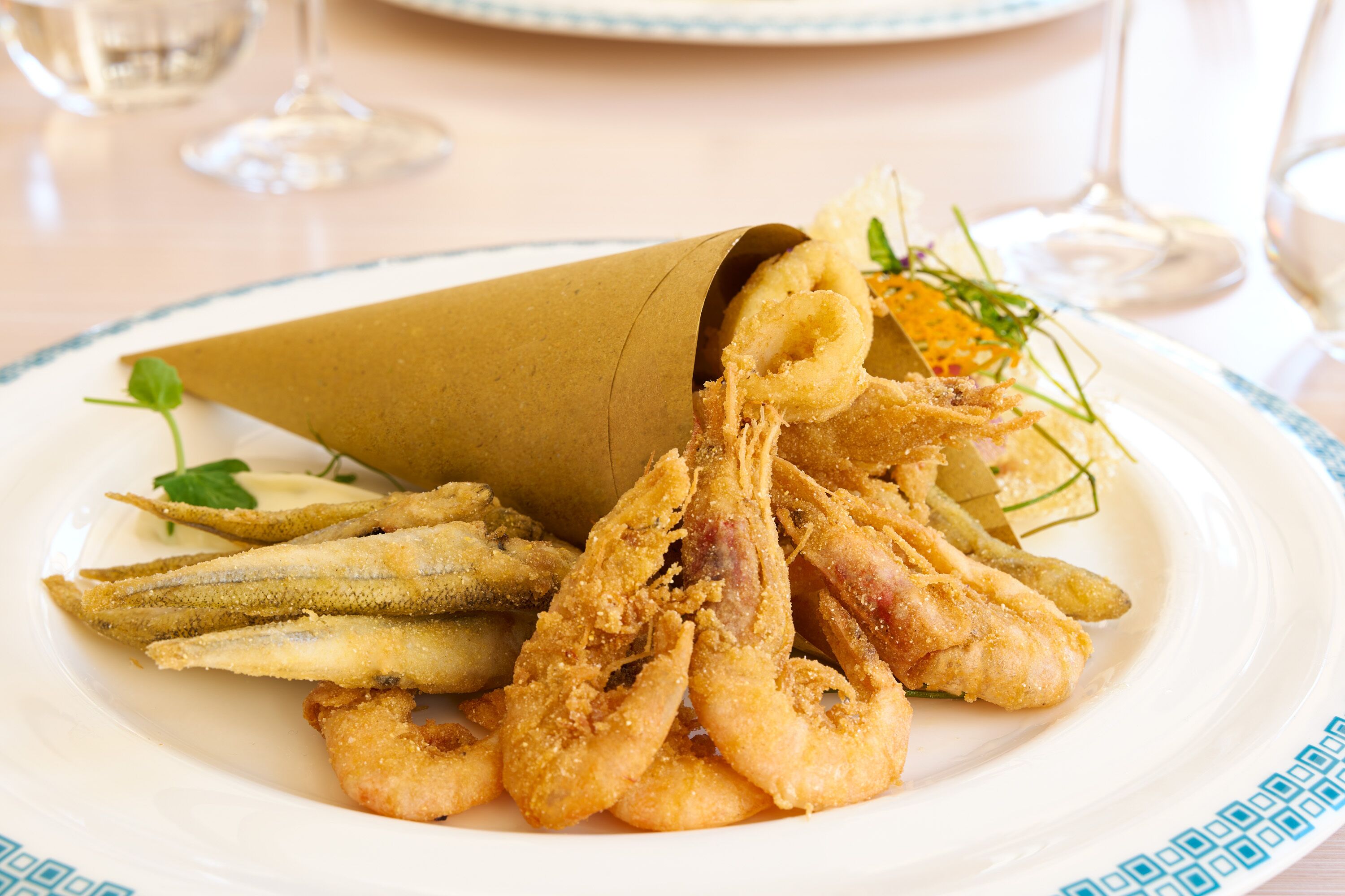 Um prato de frutos do mar fritos, incluindo camarão e peixe, acompanhado de batatas fritas e guarnecido com ervas.