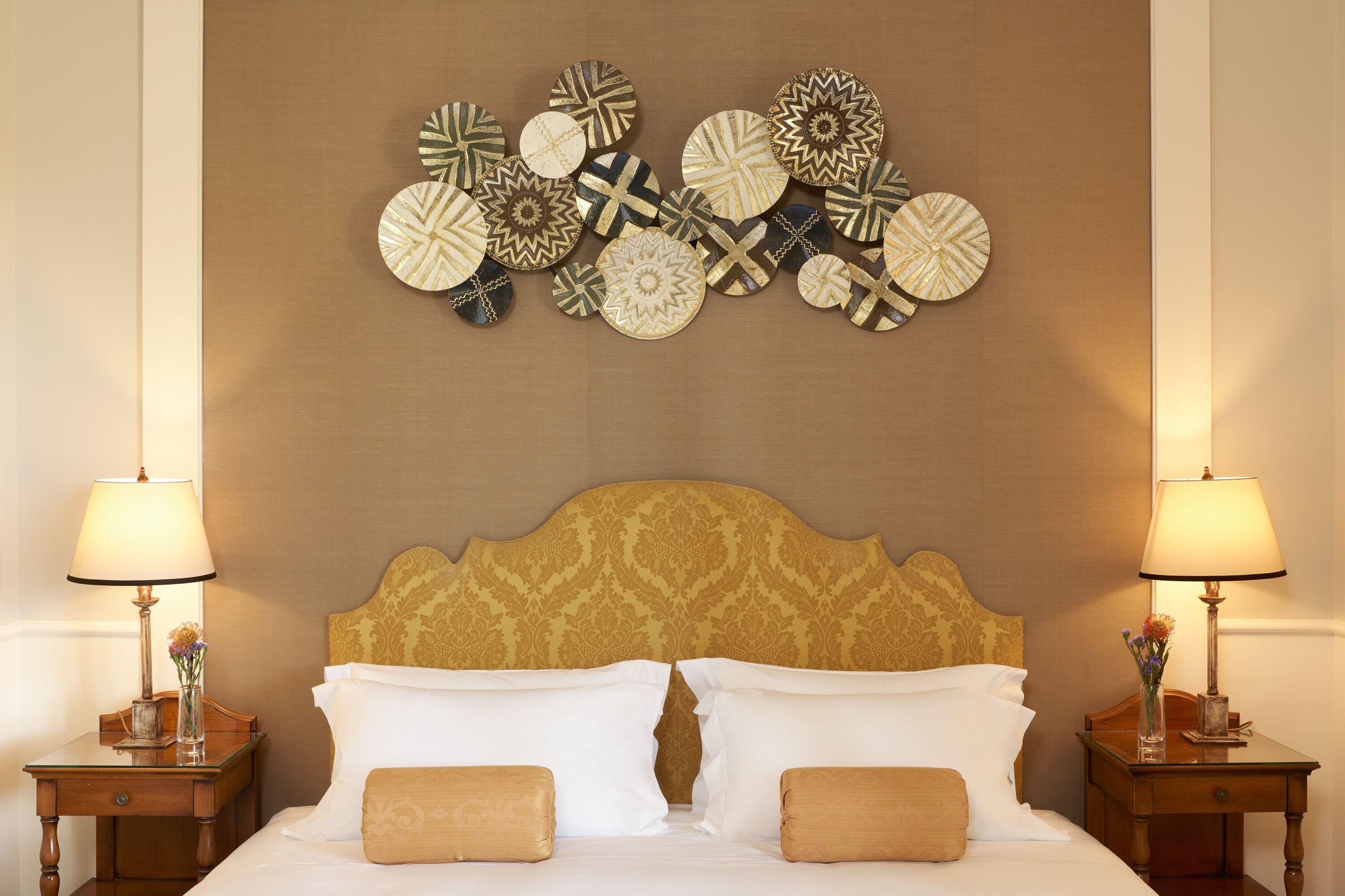 A hotel room with a large bed, two bedside tables with lamps, and a decorative wall hanging above the bed.