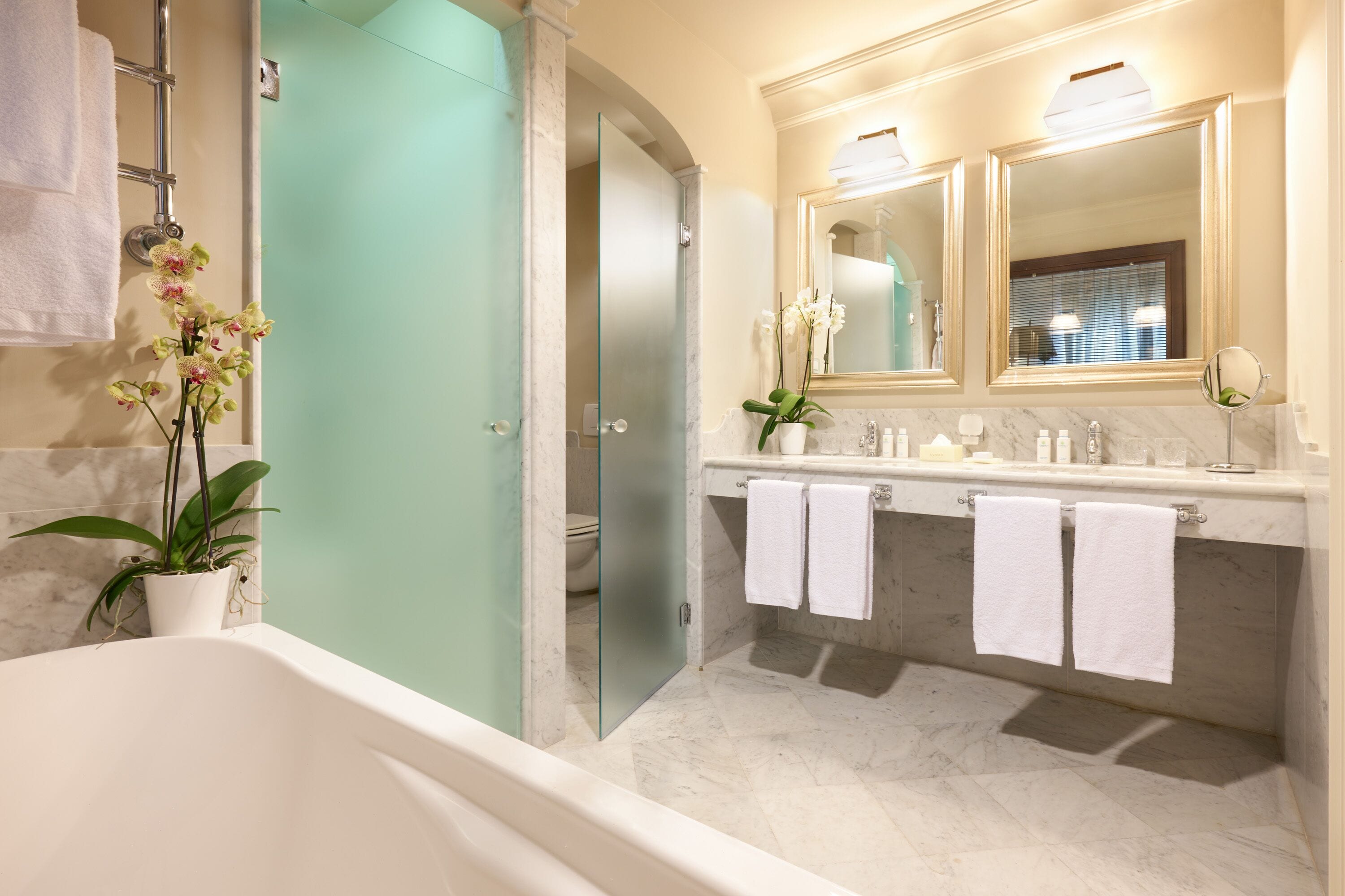 Un baño moderno con bañera, cabina de ducha de vidrio, tocador de mármol y dos espejos.