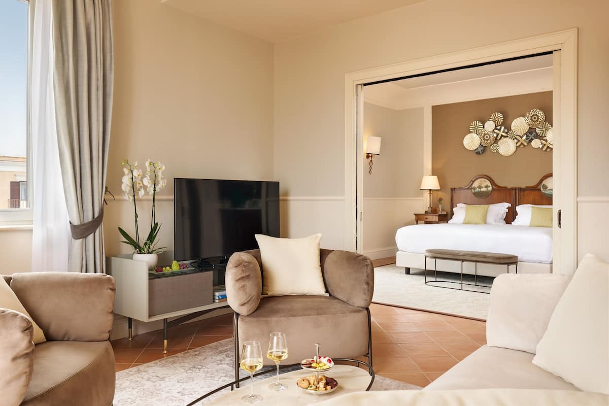 Una habitación de hotel moderna con sofá, televisor, mesa de comedor con vasos y aperitivos, cama y un adorno en la pared.