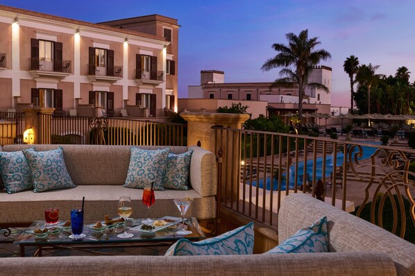 A balcony with a pool, a sofa with patterned cushions, and a table with drinks and snacks. - Almar Giardino di Costanza Mazara del Vallo Resort & Spa (Mazara del Vallo)
