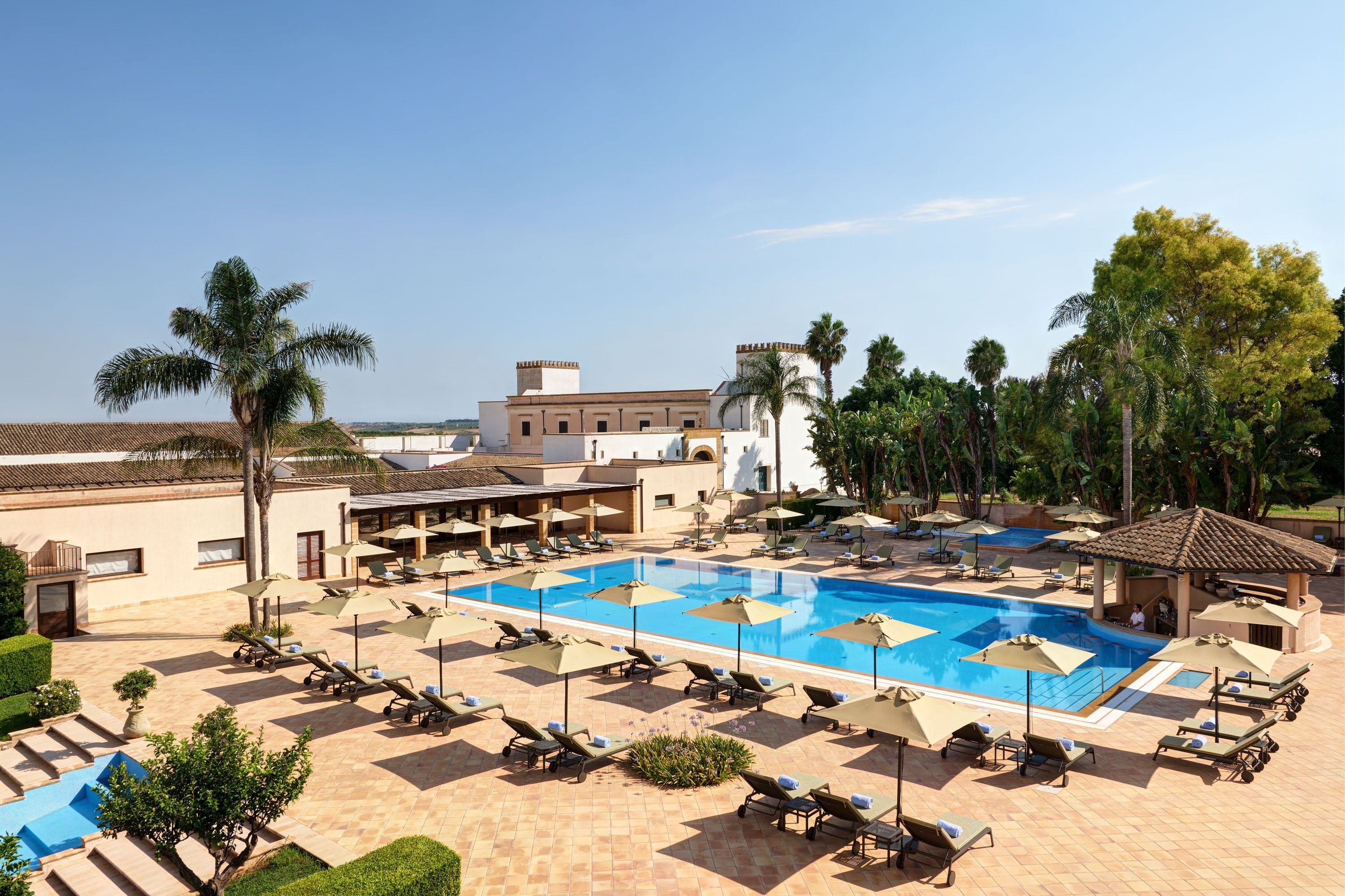 Un resort con una piscina grande, tumbonas y palmeras.