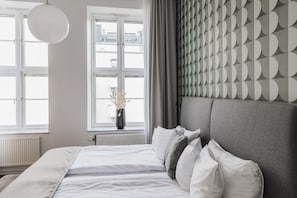 A modern bedroom with a large bed, a window with curtains, and a wall with a geometric pattern.