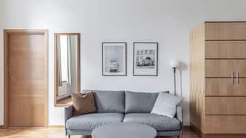 Ein modernes Wohnzimmer mit einem grauen Sofa, einem runden Couchtisch und einem Holzschrank. An der Wand hängen zwei gerahmte Bilder und ein Spiegel.